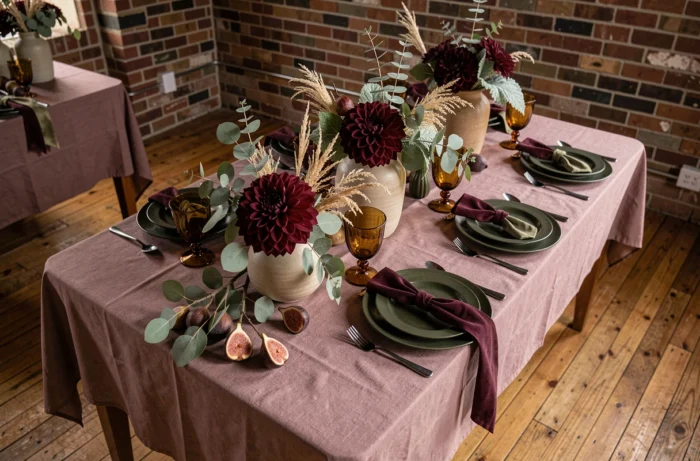 Table de mariage d'automne décorée dans une palette prune et vert olive avec des dahlias bordeaux, de l'eucalyptus et de la vaisselle ambrée